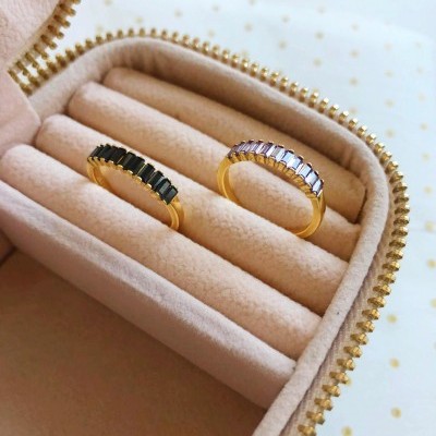 Anéis dourados com pedras preto e lilás em caixa de veludo bege com fecho zip dourado