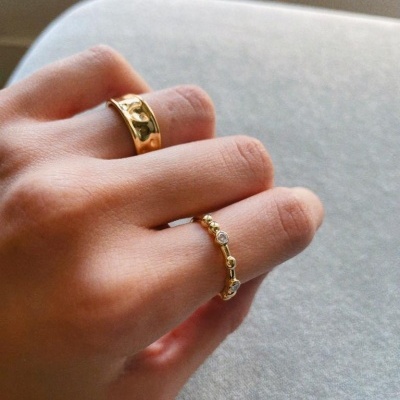 Mãos com dois anéis dourados, um largo com padrão e outro fino com pedras brancas