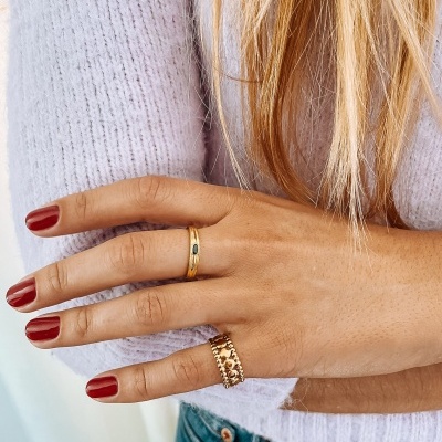 Mão feminina com dois anéis dourados e unhas vermelhas.