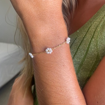 Pulseira dourada com flores de pérolas no pulso de pessoa com roupa verde