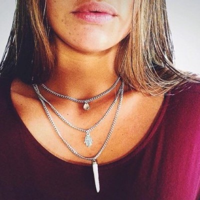 Colar feminino com três correntes prateadas e pendentes distintos sobre t-shirt bordeaux