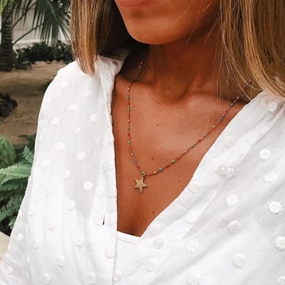 Colar feminino com pendente estrela dourado e contas coloridas usado com camisa branca texturizada