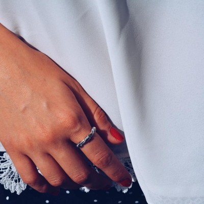 Mão com anel prateado e unhas vermelhas sobre roupa branca e roupa preta com bolinhas brancas