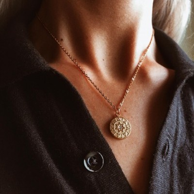 Colar dourado com pendente redondo e padrão geométrico sobre camisa preta