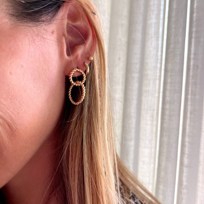 Brincos dourados de elos entrelaçados na orelha direita de mulher com cabelo loiro