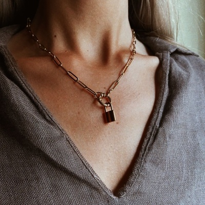 Colar dourado com elos grandes e cadeado pendurado ao pescoço