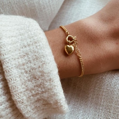 Pulseira dourada com pendente em forma de coração no pulso
