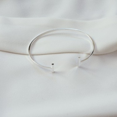 Pulseira metálica prateada aberta sobre tecido branco liso