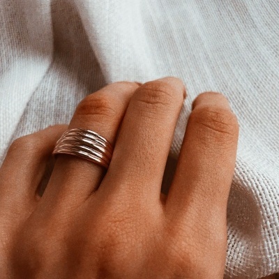 Anel prateado com cinco bandas entrelaçadas na mão sobre tecido branco