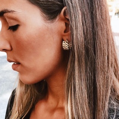 Brincos de argola dourados com textura, usados por mulher com cabelo castanho claro