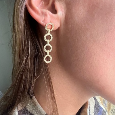 Brinco dourado pendente com círculos brilhantes na orelha de mulher