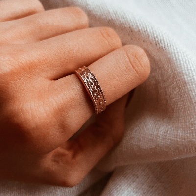 Anel metálico com padrão recortado num dedo sobre tecido branco