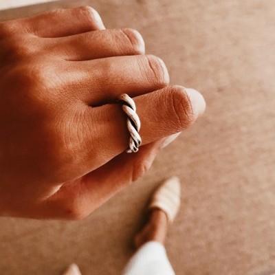 Anel prateado entrelaçado numa mão sobre tapete castanho