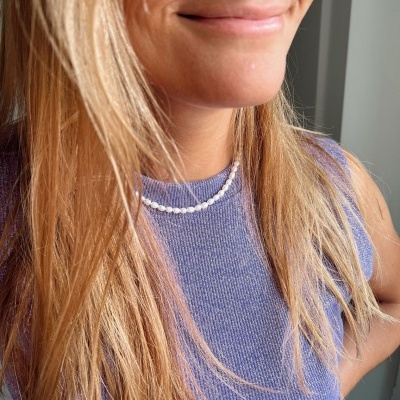 Colar de contas brancas em mulher com blusa roxa