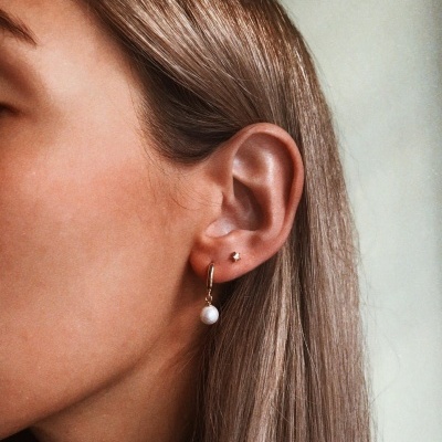 Rosto parcial com brincos dourados e pendente de pérola na orelha esquerda