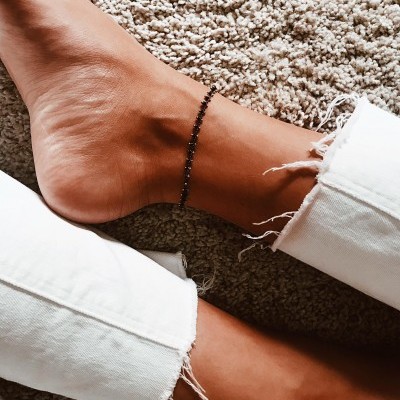 Pulseira de contas pretas no tornozelo com calças brancas e tapete bege