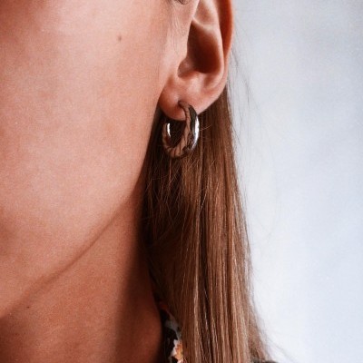 Brinco de argola pequeno prateado numa orelha feminina