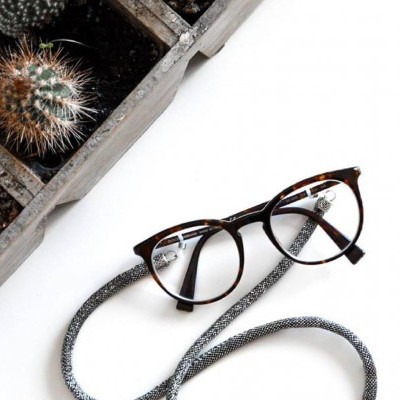 Óculos de grau com armação castanha e alça trançada cinzenta junto a cacto em vaso de madeira