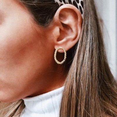 Brincos de argola dourada texturizados em mulher com camisola branca e fita de padrão castanho no cabelo