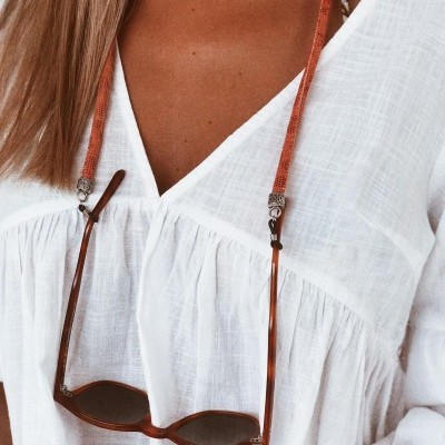 Pessoa com blusa branca e óculos de sol castanhos suspensos por fita