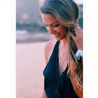 Mulher com vestido preto e colares dourados em ambiente ao ar livre.