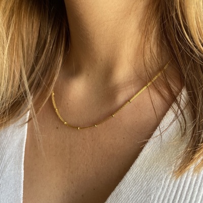 Colar dourado fino com pequenas esferas numa pessoa com camisola branca