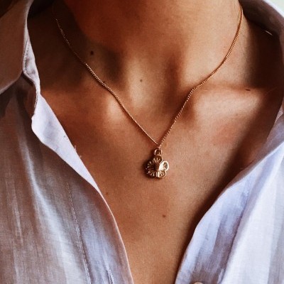 Colar dourado com pendente de flores usado com camisa branca