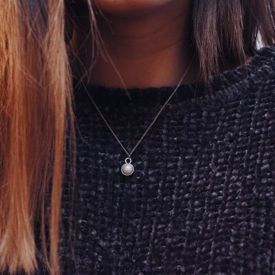 Colar com pendente redondo com pedra branca, usado sobre camisola preta