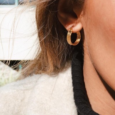 Brinco de argola dourado com textura riscada na orelha de uma pessoa