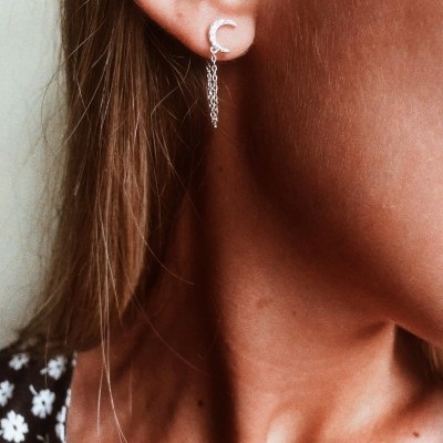 Brinco prateado em forma de meia-lua com correntes penduradas na orelha