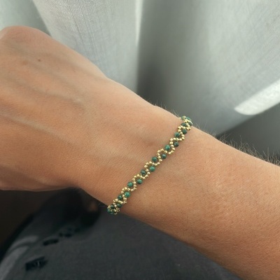 Pulseira trançada com contas verdes e douradas no pulso
