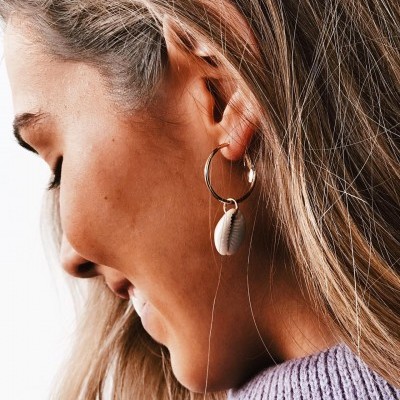 Brinco de argola dourada com pendente de concha branca na orelha
