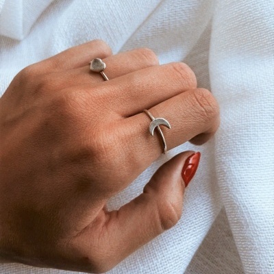 Mão com anéis prateados em tecido branco.