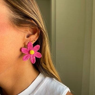 Brinco grande em forma de flor rosa com centro amarelo numa orelha feminina.