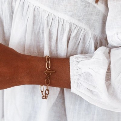 Pulseira dourada de elos no pulso com blusa branca de manga bufante