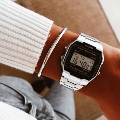 Relógio digital Casio prateado com bracelete em aço inoxidável no pulso com pulseira fina e roupa branca e jeans cinzento