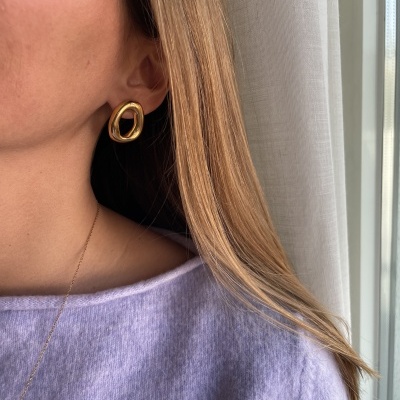 Brinco dourado irregular com roupa lilás e fundo de cortina branca