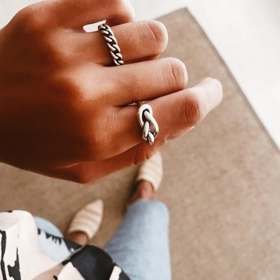 Mão com anéis prateados e fundo com tapete castanho e chão claro