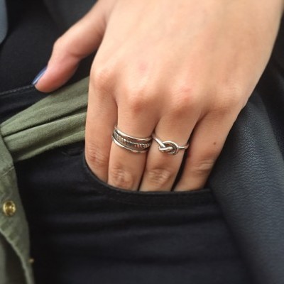 Mão com anéis prateados em bolso preto de roupa verde