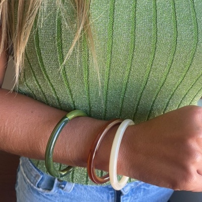 Pulseiras de resina verde, castanho e branco no pulso de uma pessoa com top verde e calças de ganga.