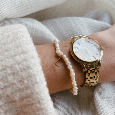 Relógio dourado com pulseira metálica e pulseira de pérolas no pulso