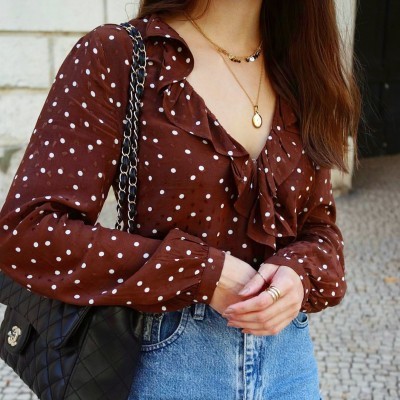 Blusa castanha de bolinhas brancas com folhos, calças de ganga azuis e mala preta com corrente