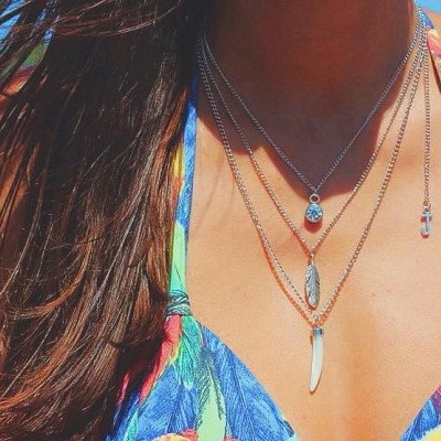 Três colares femininos prateados com pendentes sobre pele bronzeada e roupa de banho colorida.