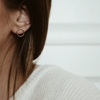 Brinco argola dourada no ouvido de mulher com camisola branca