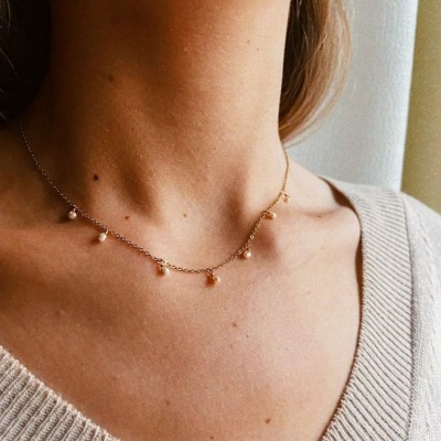 Colar dourado com pérolas usado por pessoa com camisola bege