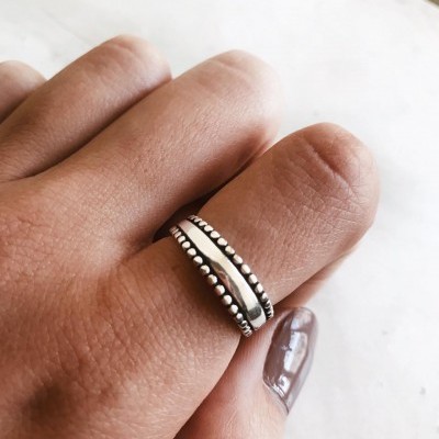 Anel prateado com bordas em bolas no dedo anelar de uma mão com unha castanha