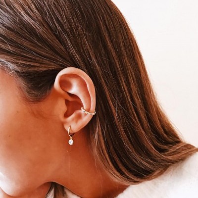 Perfil esquerdo de mulher com dois brincos dourados na orelha e fundo branco.