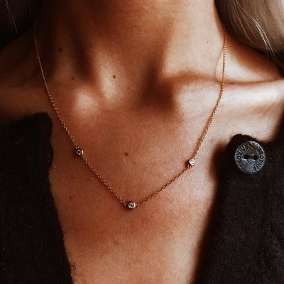 Colar dourado delicado com pedras transparentes usado com camisola preta de malha