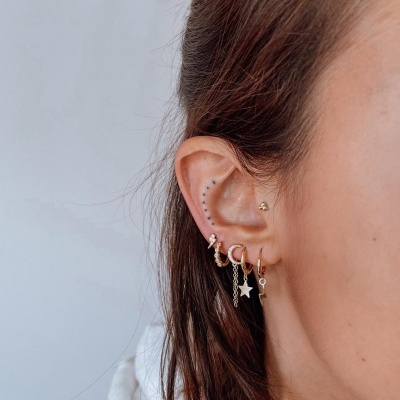 Orelha feminina com brincos dourados variados em fundo cinza claro