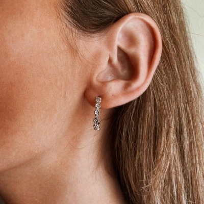 Brinco prateado tipo argola pequena com textura facetada na orelha de mulher de cabelo castanho claro